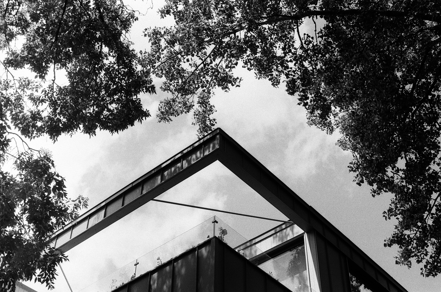 view looking up
at the corner of a weird bit
of a house's balcony type thing.
the top edge of the roof
extends over the edge of the inset balcony.
I have no idea how to explain it.
there are trees around it
and sky behind it.