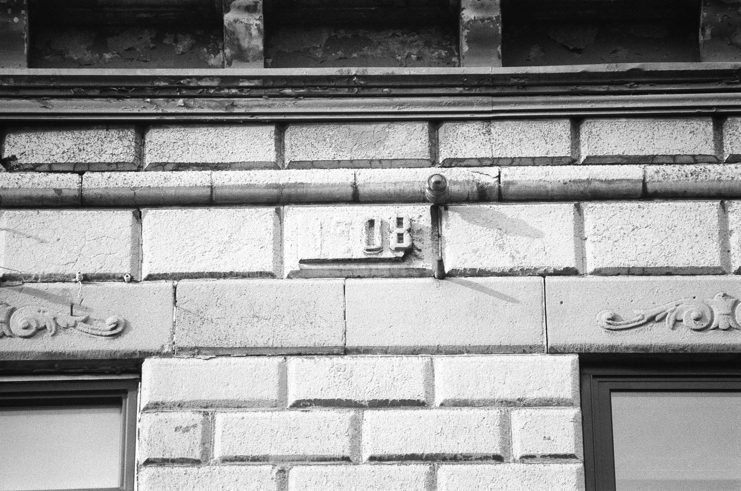 the side of a brick building
centred around the brick
bearing the erection year.
the raised portions of the 19
have fallen off,
and only the 08 is left.
above this is the edge of the roof
and below it are two ornamental bricks
at the tops of windows.