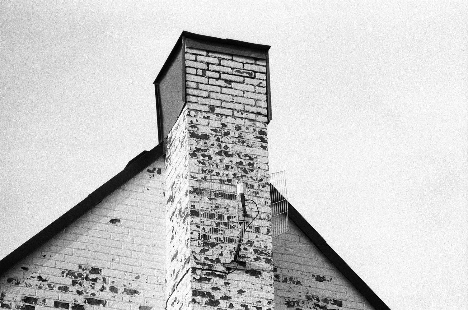 the column of bricks
that was once a chimney
on the side of a triangular roofed house.
the bricks are painted a light colour
but it is peeling in many places.
there is one of those wireframe
rectangular sort of satellite dish things
on the side of the column.