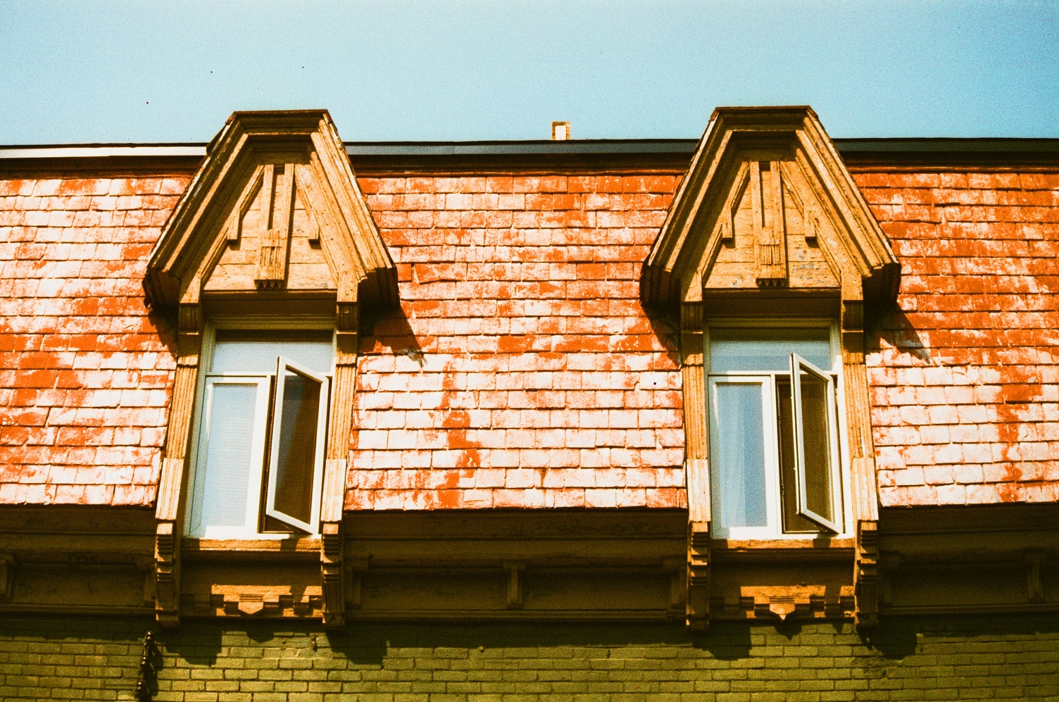 two windows at the top of a plateau building.
the base of the building is green brick
and the top roof part is orange shingles
that appear very shiny in this photo.
the windows set into the shingled part
have big flattened triangle
thingies on top.
made of wood, you know.