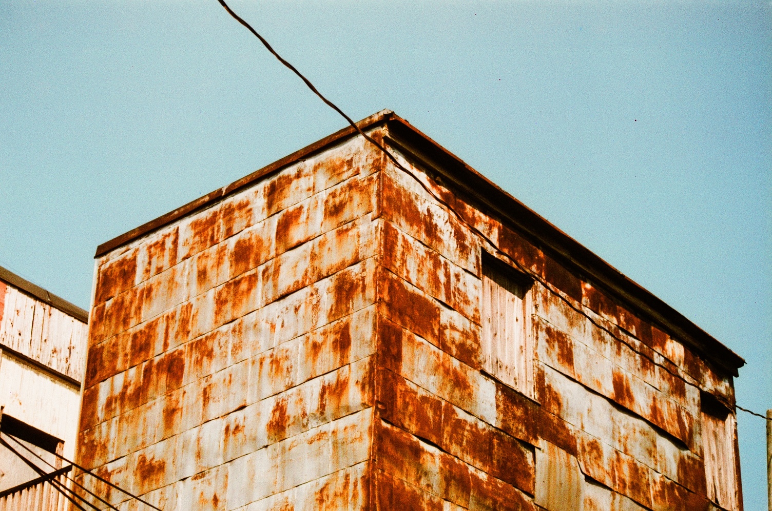 a building extension
whose exterior walls
are made of severely rusting metal.
the building is viewed from its corner,
looking at its top
against a blue sky.