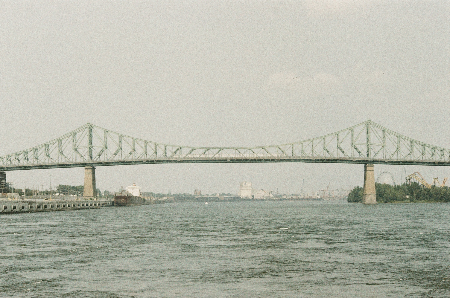 the jacques-cartier bridge
viewed from a perpendicular angle,
right at the middle of it.
a roller coaster can be seen behind it on the right
and a cargo boat on the left.