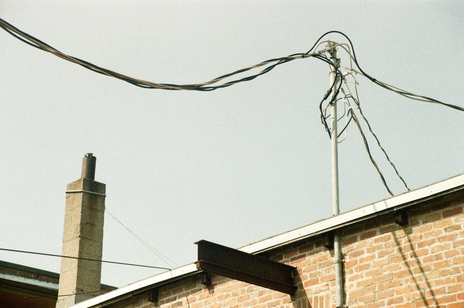 the top edge of a building,
including power line pole
on the roof,
metal beam sticking out the side,
and a little stone chimney.