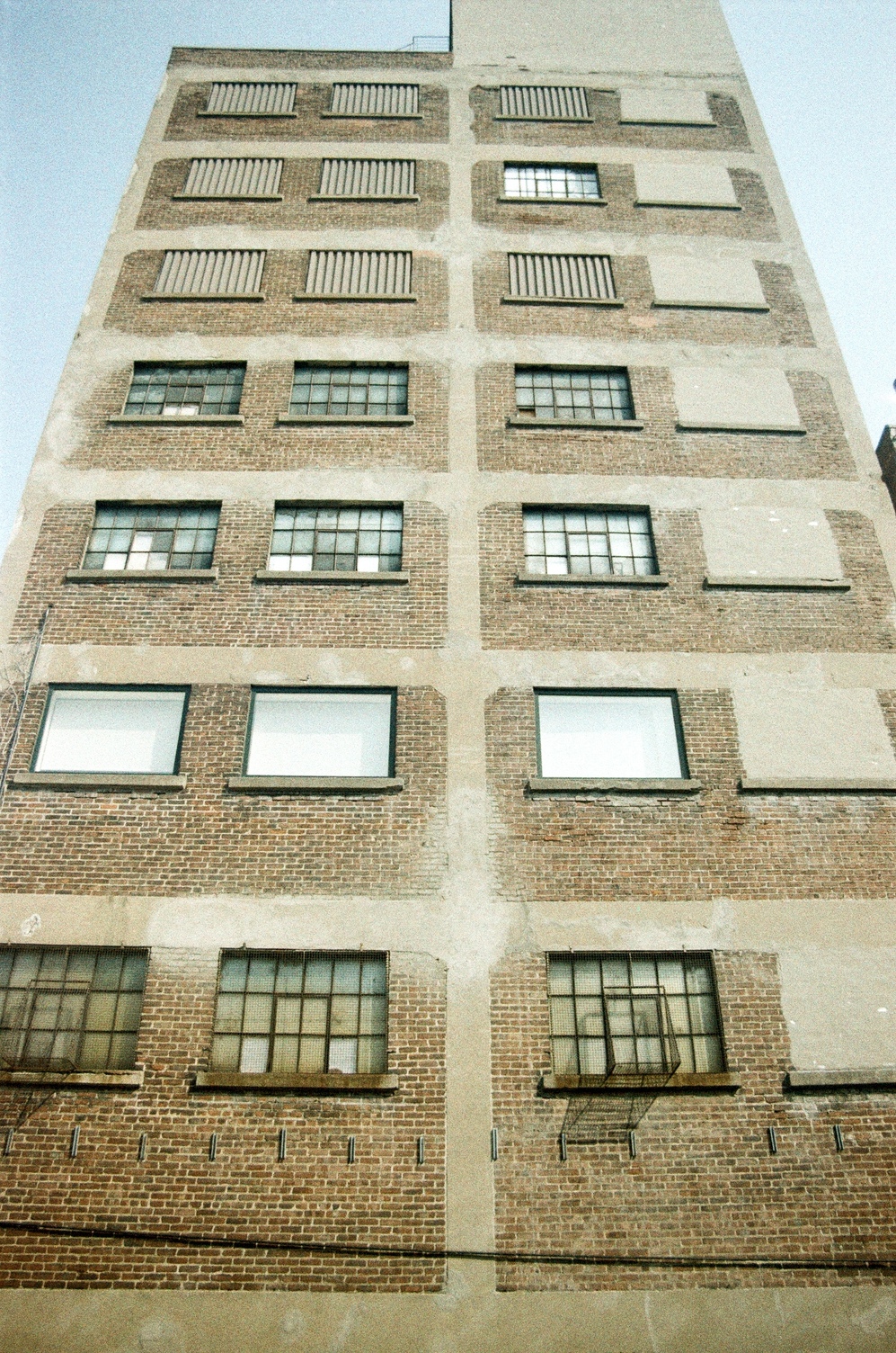 a view all the way up the side
of an old brick factory building,
7 storeys tall.
all of the windows on the far right
have been filled in with cement.
some of the other windows
have been filled in with
what looks like corrugated metal.
some of the remaining windows
are the original 6x3 pane
and some are single pane.