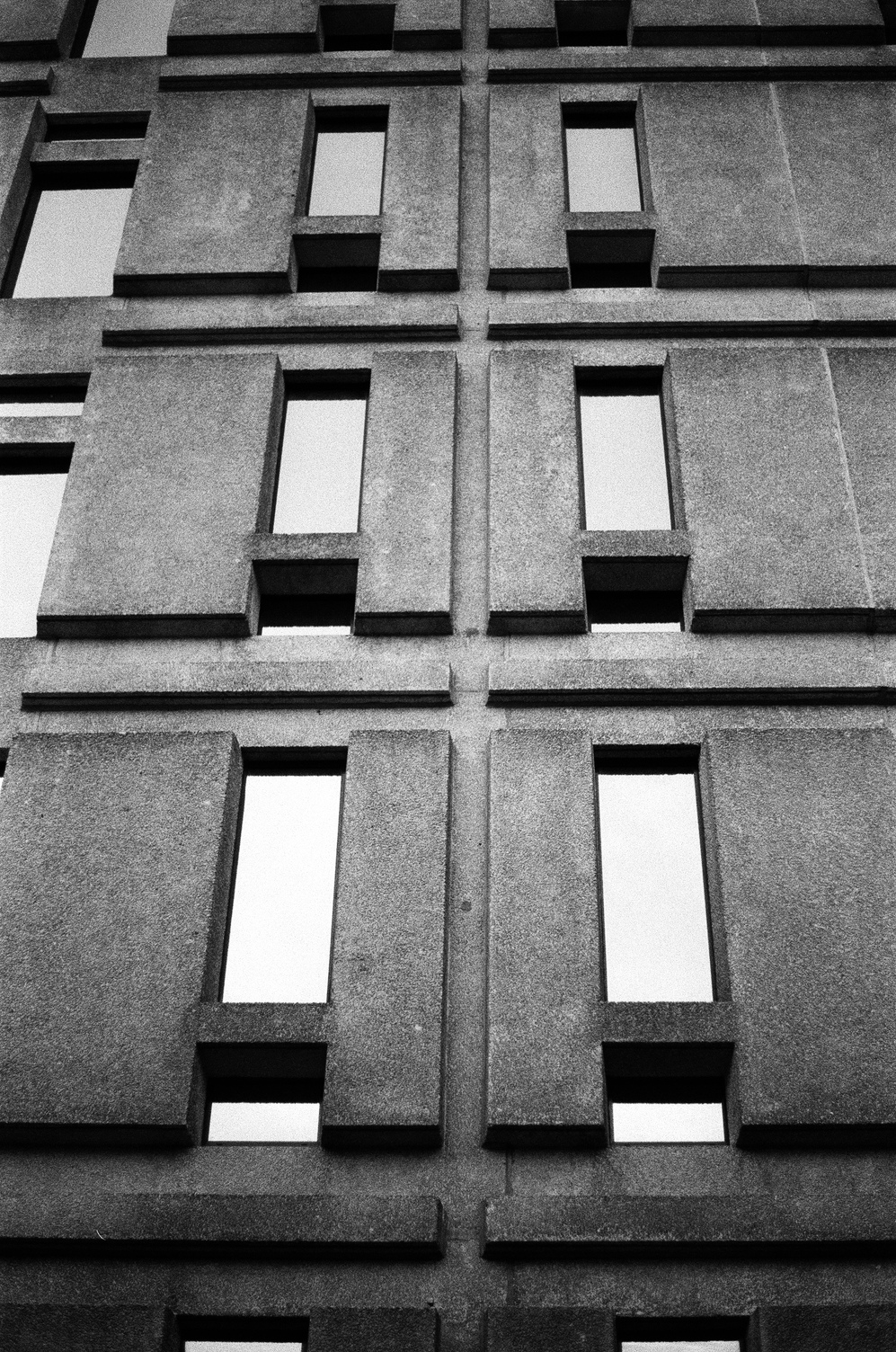 the side of a concrete building
with an intricate pattern
of concrete and narrow windows.
the windows are reflecting a light sky.
good contrast and shadows here.