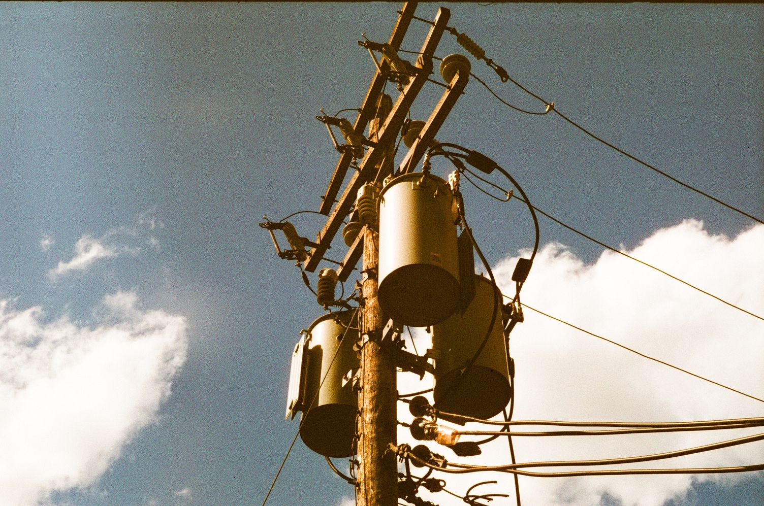 power lines atop a wooden pole with 3 drums
against a blue sky with white clouds.