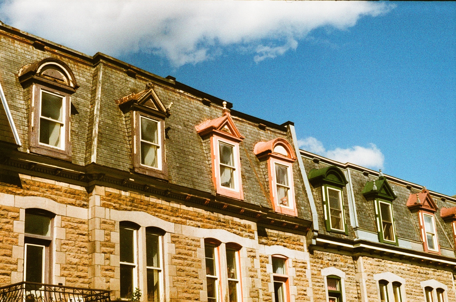 the top halves of some classic plateau rowhouses
against a light blue sky with some clouds.
the top windows are painted in a sequence of
dark purple, orange, dark green, some kind of red.