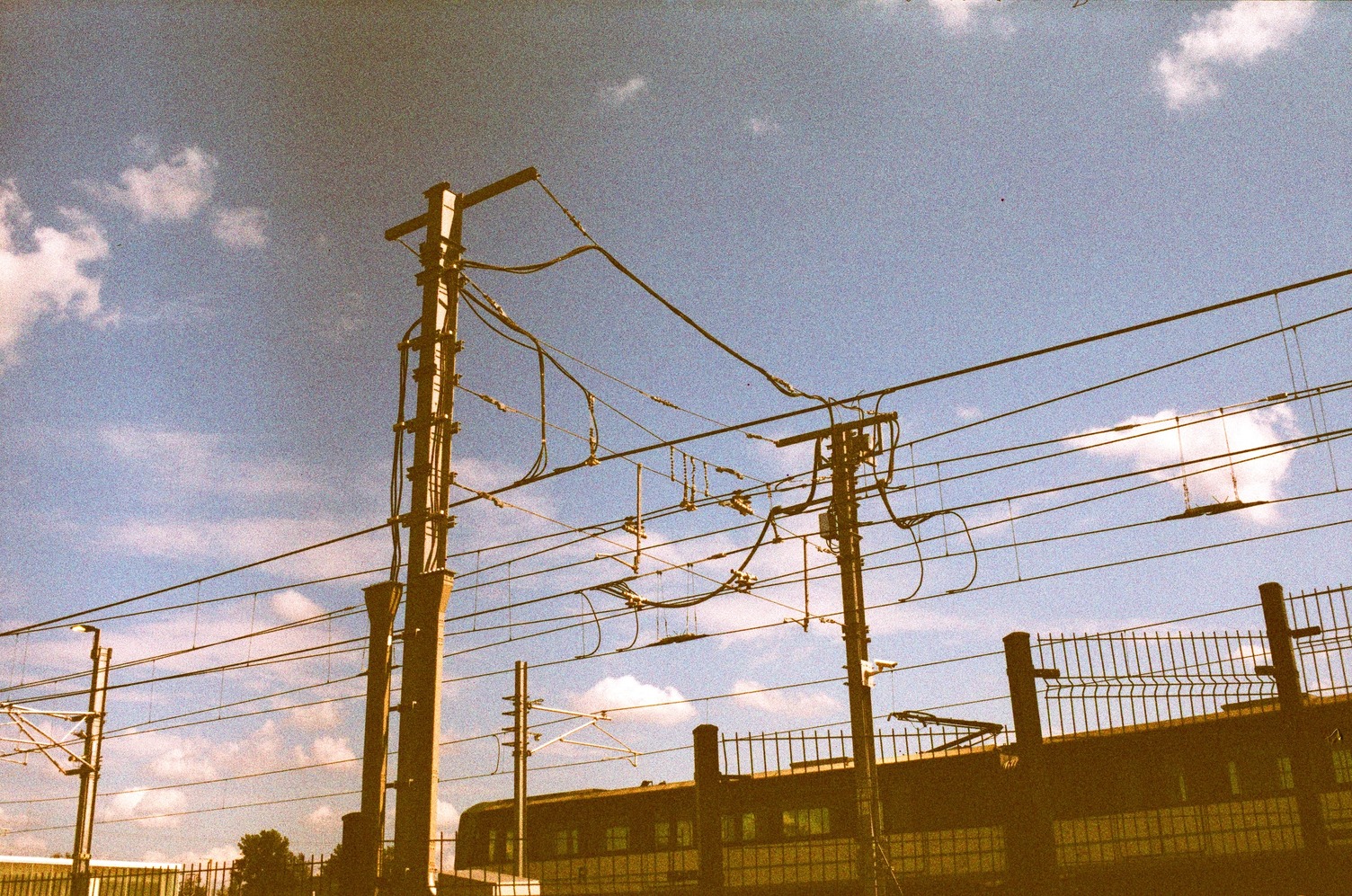 overhead lines for electric trains
silhouetted against a blue sky
with sparse clouds
as a train goes past.