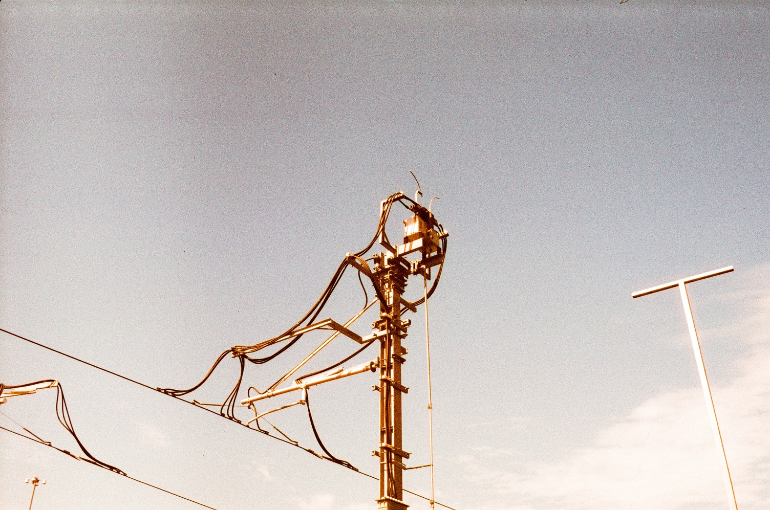 some sort of device atop
overhead lines for electric trains
against a grey-blue sky.