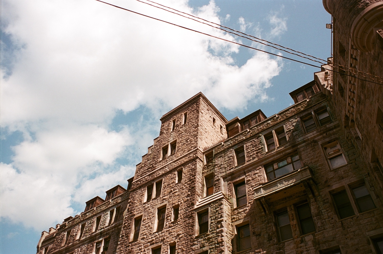 view up at a huge old stone building
with lots of 3D shape going on
and lots of windows.
past it is a blue sky
with a big white fluffy cloud.