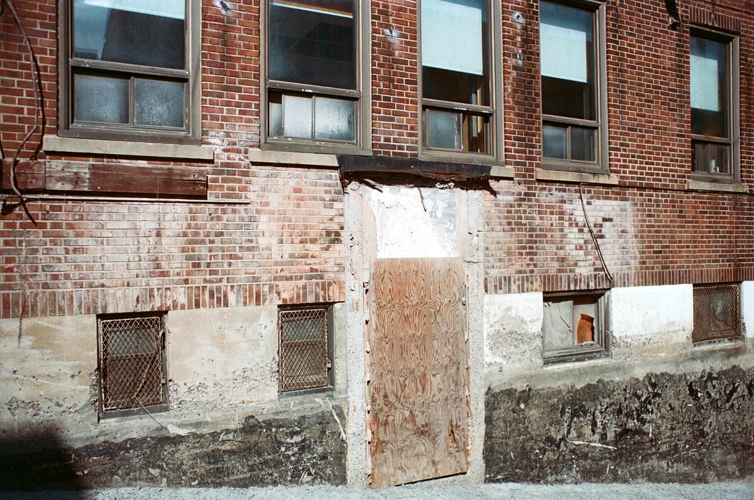 the back of an old brick building
that is probably being renovated.
the ground is descending
behind the building as if to underground parking,
and there is a space for a door
that is blocked with plywood.