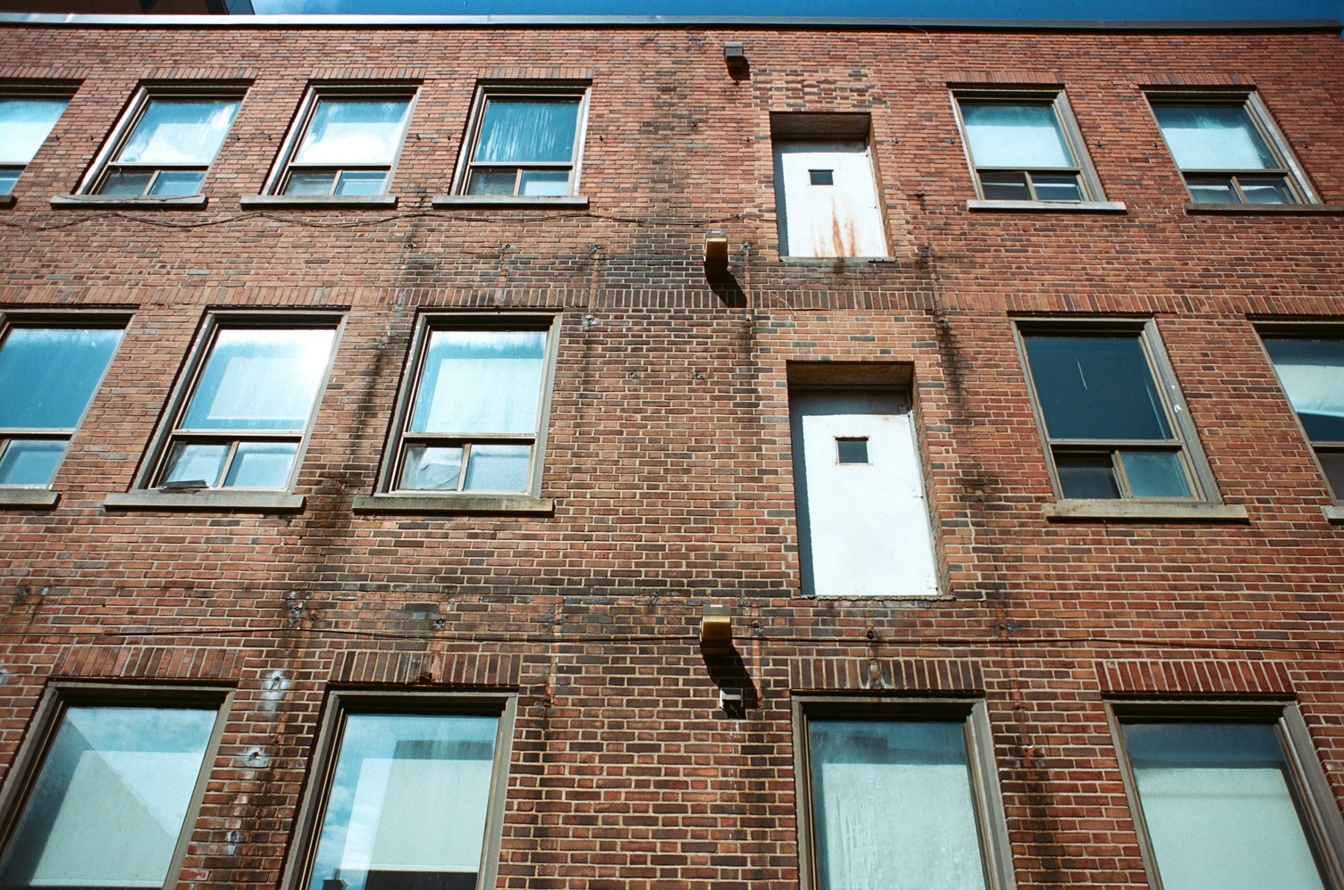 looking up at an old red brick building
from the ground.
there are three rows of windows.
there are also two doors
with no handles and little square windows
that would open onto nothing.