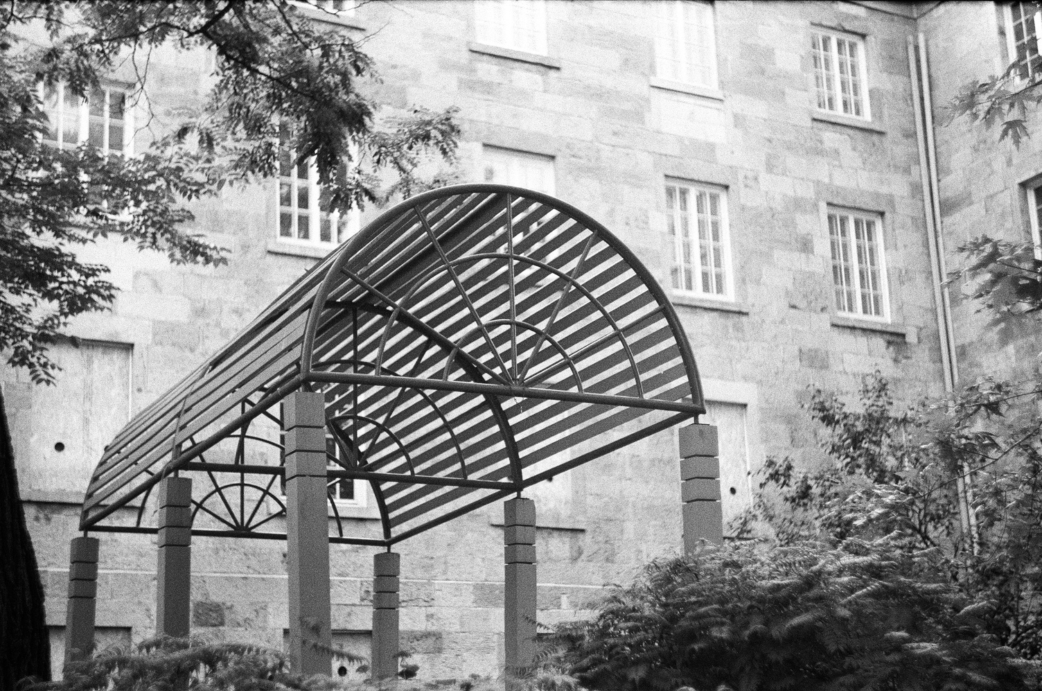 a metal frame structure
in the shape of half a cyllinder
suspended,
presumably over a walkway,
on square concrete pillars.
the pillars have three notches
in them near the top.
this is just outside a large stone building.