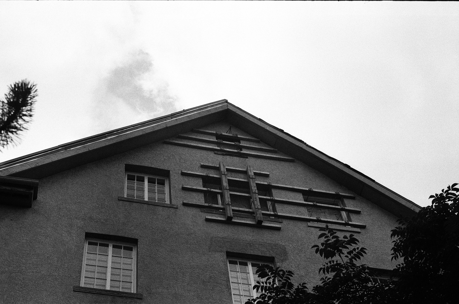 the top of a large building
with a pointed roof.
some of the windows are intact
while some have beams of wood
across them on the outside
seemingly holding boards of wood
against the insides?