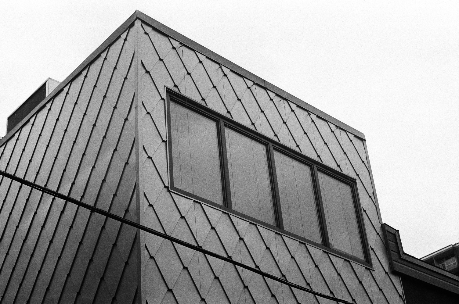 a weird cube of building
covered in a metal diamond tiling pattern
with one wide window in the side
and some cables under tension
going down it.