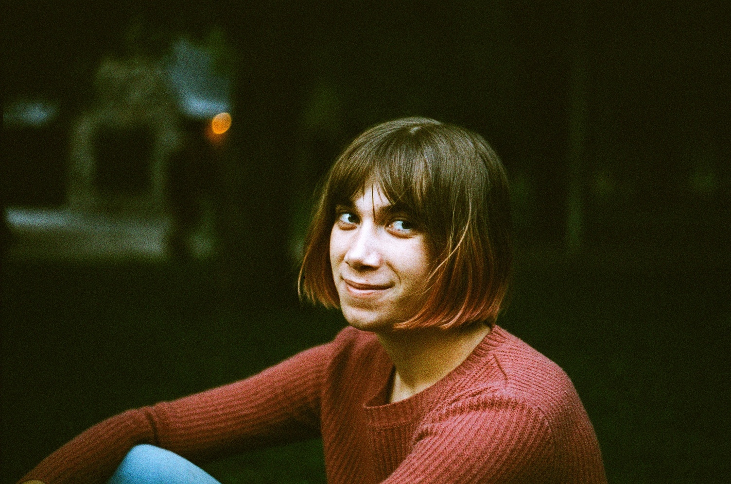 Ayla in an orange sweater
looking to the side and smiling.