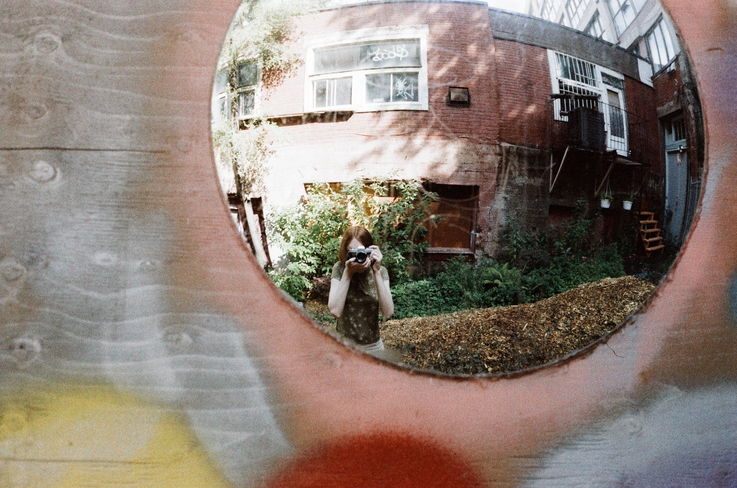 a selfie in a convex mirror.
the mirror is off to the top right.
I'm wearing a green shirt.
behind me is a somewhat decaying
short brick building.