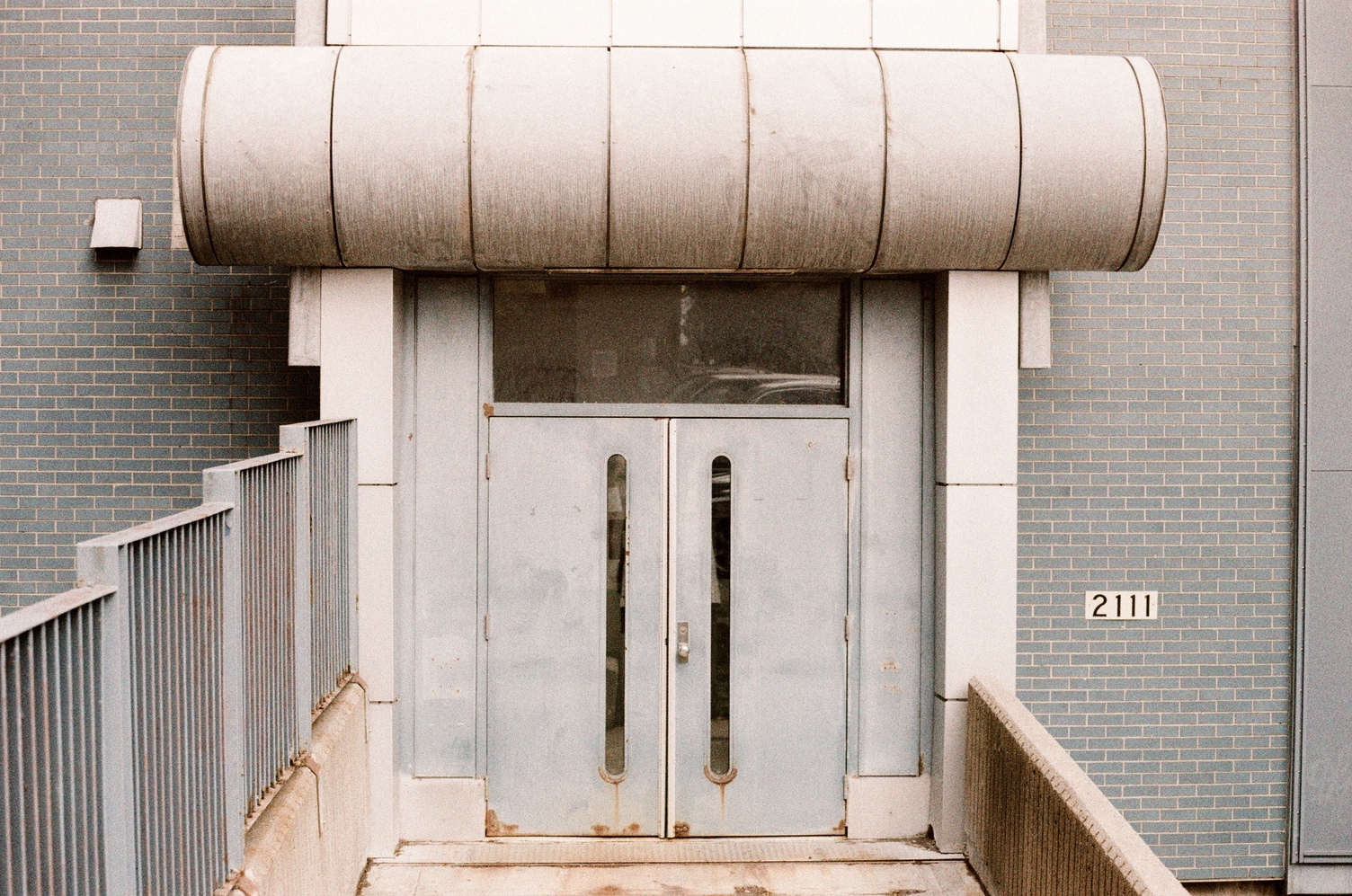 a set of metal doors
in a blue brick building
with what looks like a big duct pipe
above them.
it's not attached to anything
it's just sitting over the doors
like a giant unibrow.
there is a little bridge leading towards the doors.
to the right of the doors
is the address number 2111.