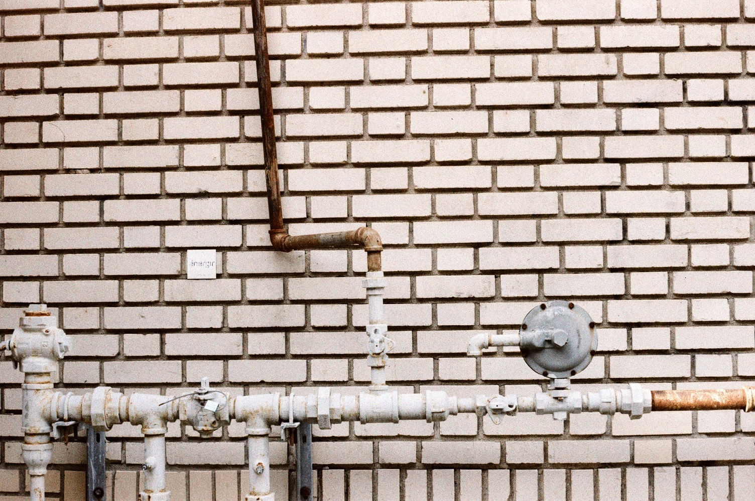 natural gas pipework
on a beige brick wall.
there is a line of pipe
going horizontal across
the bottom of the frame,
with one pipe coming off
in the middle
and going upwards,
with a zig-zag
and then continuing up at an angle.