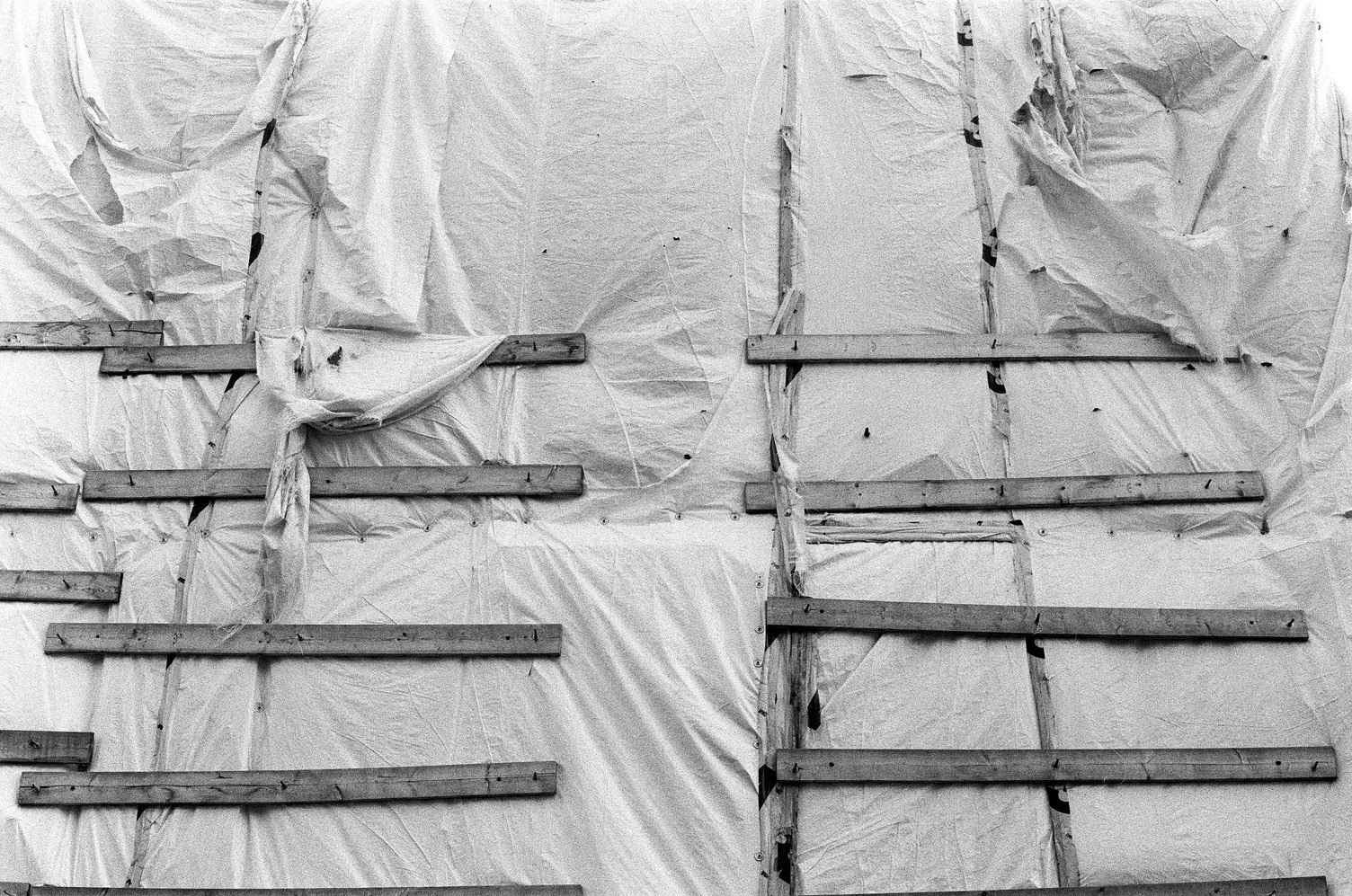 the side of a building
that's been covered in
some sort of construction fabric,
perhaps tyvek,
then had horizontal boards of wood
nailed over it.
the fabric is torn in places
and hanging down over itself.