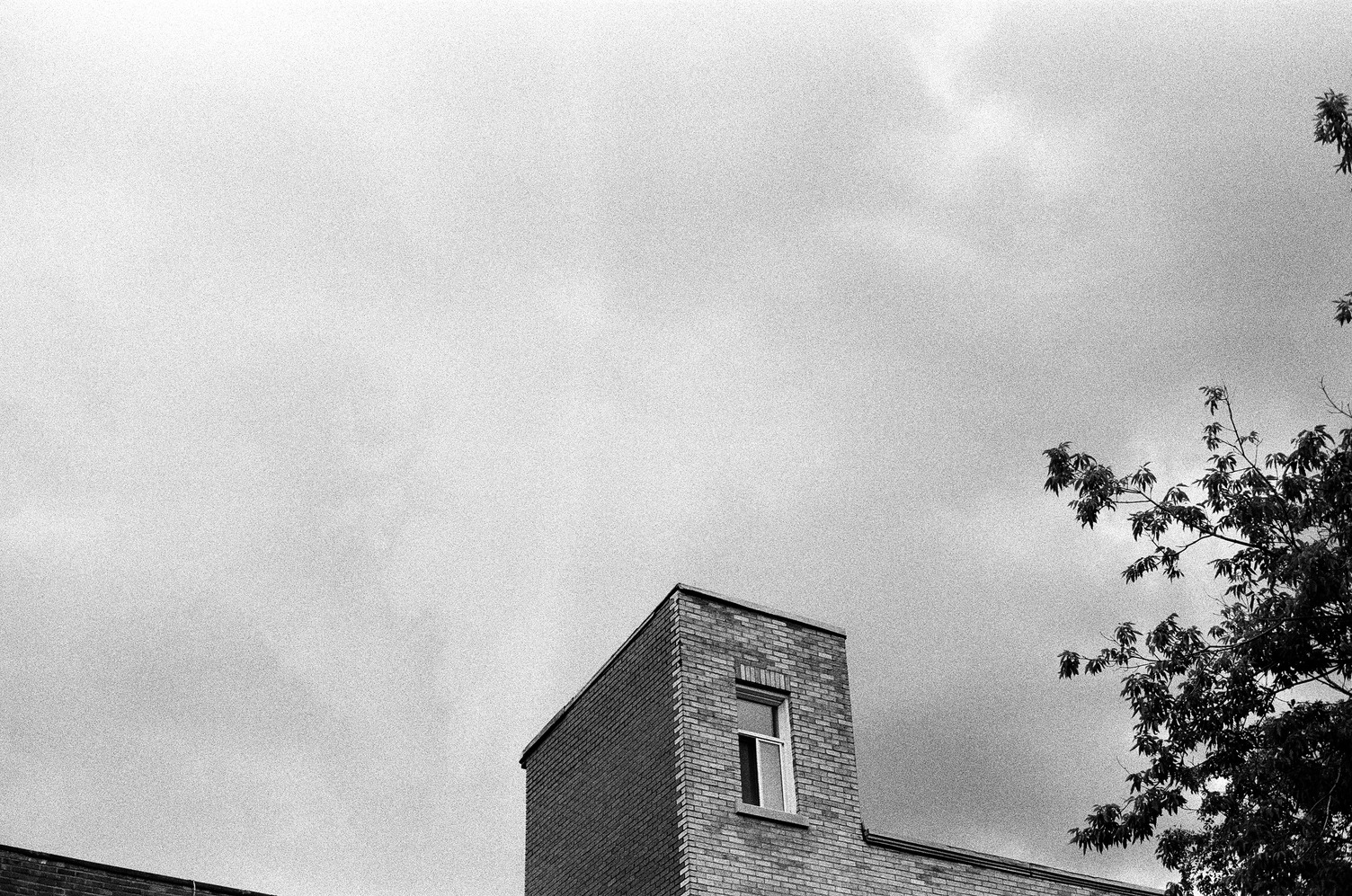 the top of a building
where a weirdly small
cube sticks up above
the rest of the roof,
with a full size window
in the side.
cloudy sky behind the protrusion.