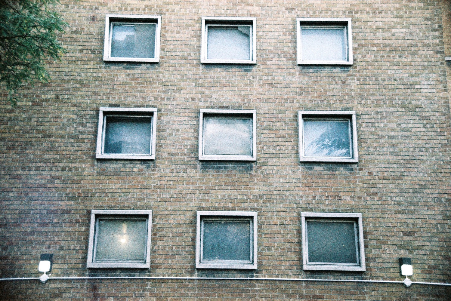 nine small square windows in a grid
on a brown brick wall.
a conduit runs under them
with a light on either side.