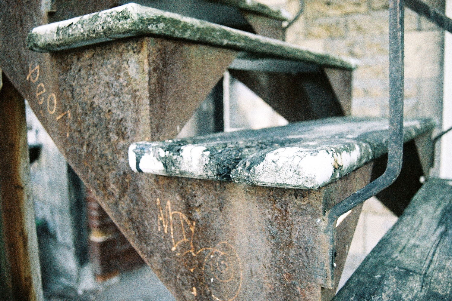 a closeup of some old walkup stairs.
the metal frame of the staircase is rusted
and the wooden steps are decaying.
they were once painted but almost all of it has come off.