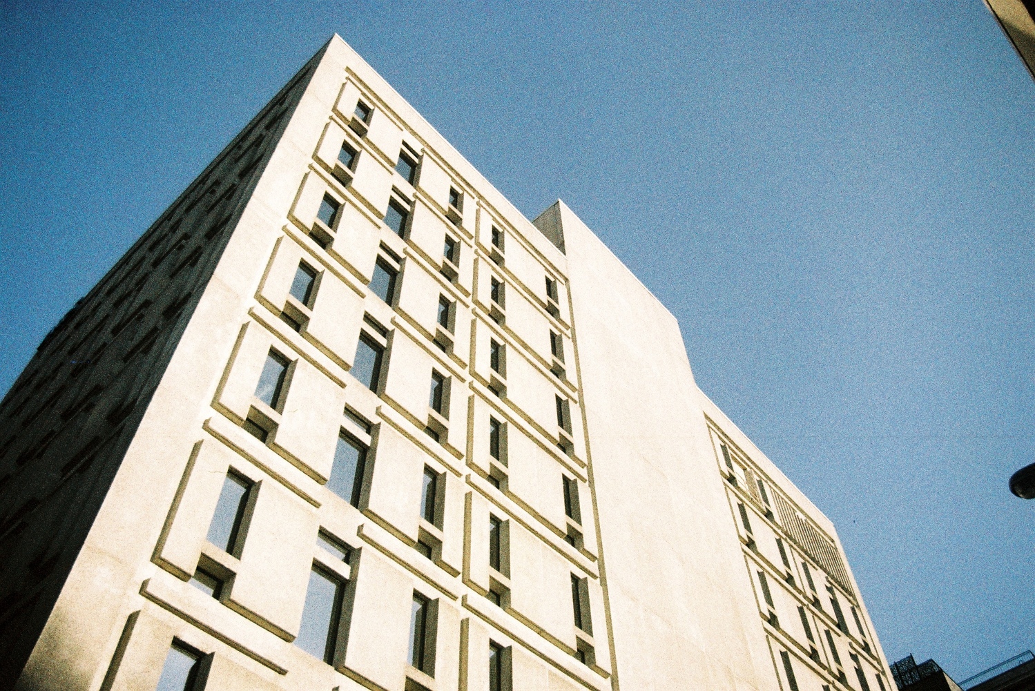 looking up at a concrete building in the sun.
it's got a detailed pattern of depth
around the windows.
the sky is blue.