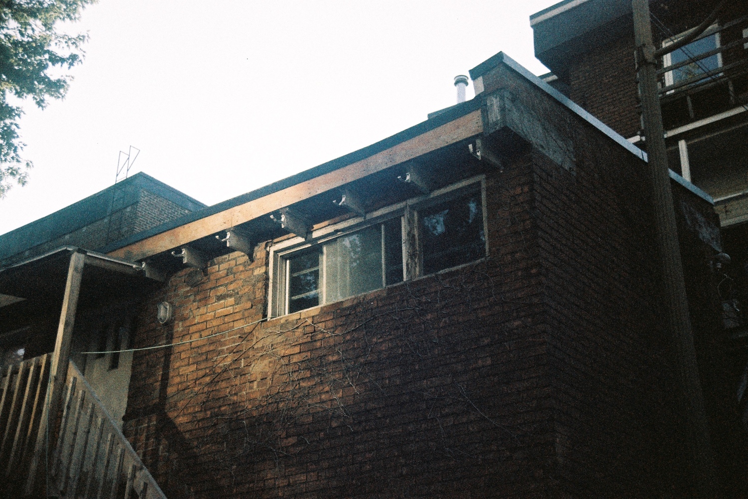 the back of something like a building over a garage,
with a high short window
and a door with some steps leading down.
the building is mostly in shadow
except an area on the left side of the window,
where the sun must be reflecting off something,
given the orientation of this particular building
and the time of day.