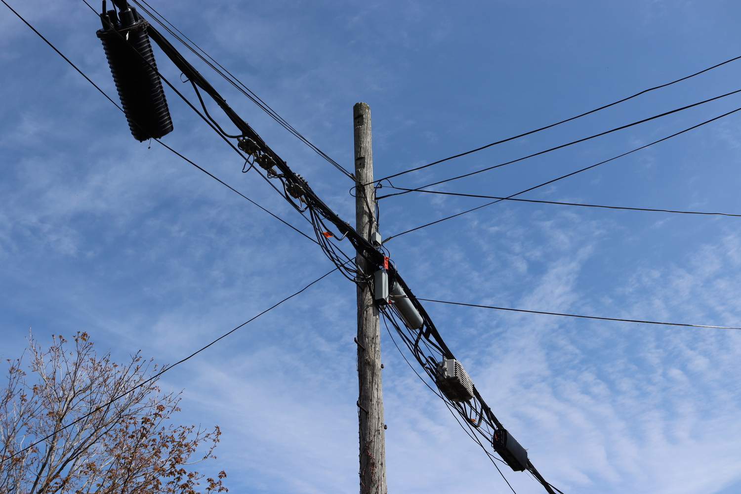 a telephone pole
against a blue sky with some light clouds,
cables coming off it in each diagonal.