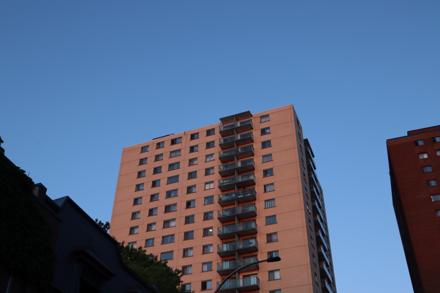 a high-rise apartment building
during or maybe just after sunset.
in the light it appears beige.
there is a row of balconies
going up the side of the building,
off-centre.