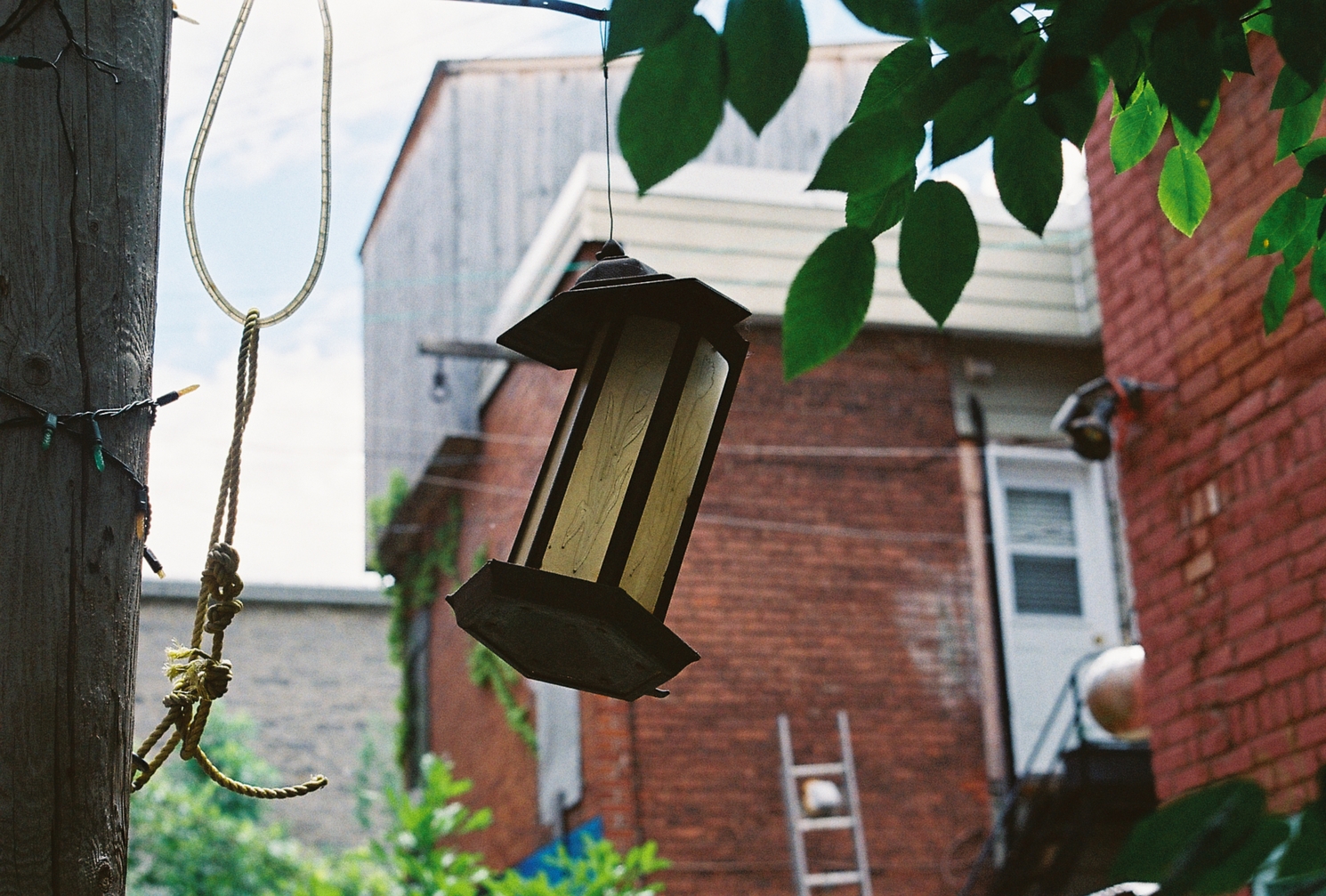 an askew lantern hanging
next to a telephone pole.
it's hanging by its hat,
but its body is crooked.
there's some rope hanging next to it,
and there's some christmas lights
looped around the telephone pole.